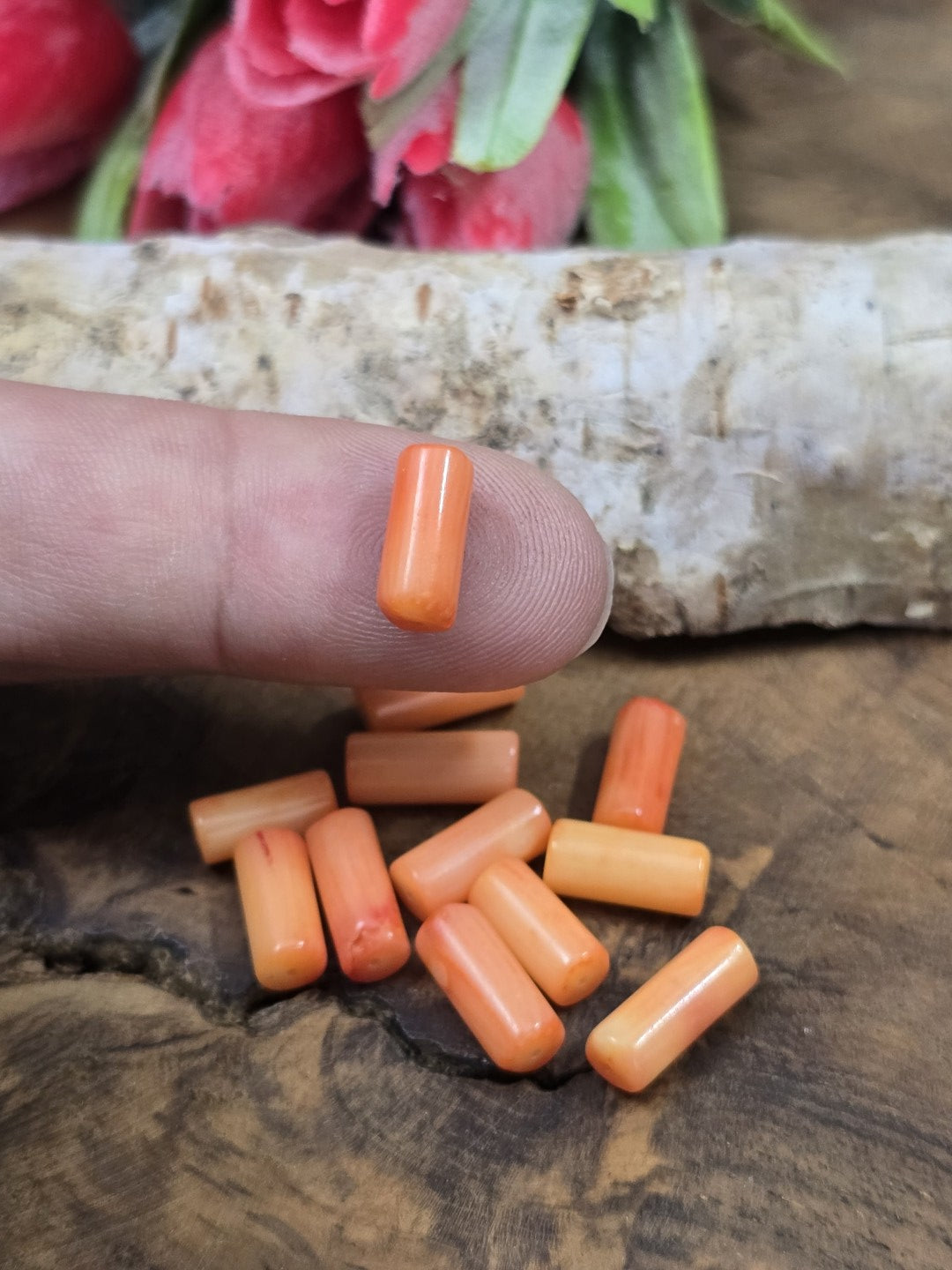 Eine lachsfarbene Korallen-Walzenperle auf der Fingerkuppe als Größenvergleich für DIY-Schmuckprojekte.
