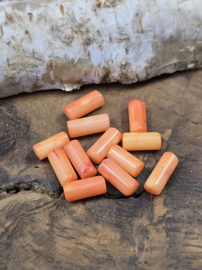 Nahaufnahme von orange-lachsfarbenen Korallenperlen in Zylinderform für handgefertigten Schmuck.