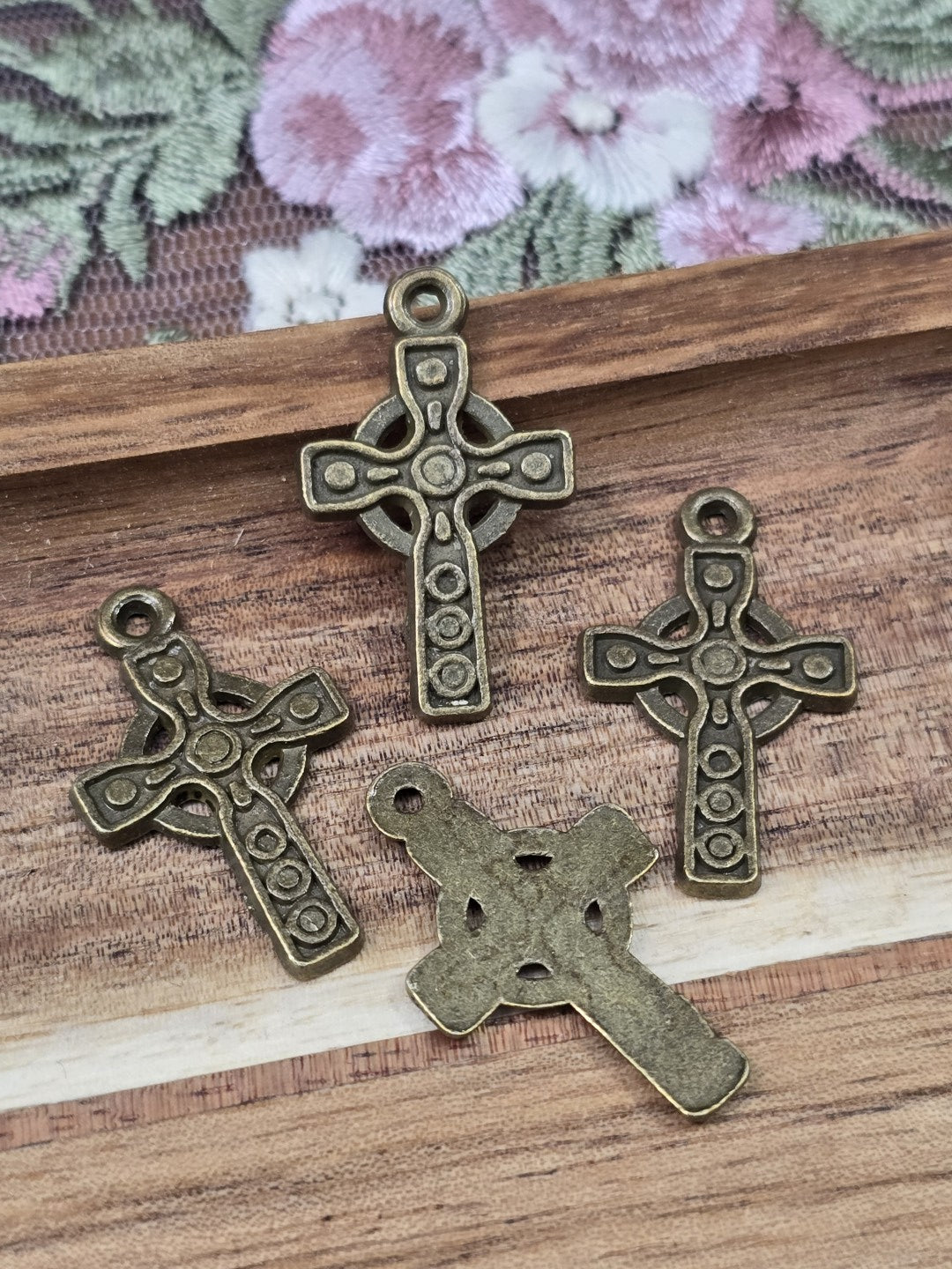 Vier keltische Kreuz-Anhänger in Antikbronze von Vorder- und Rückseite flach liegend auf Holzgrund.
