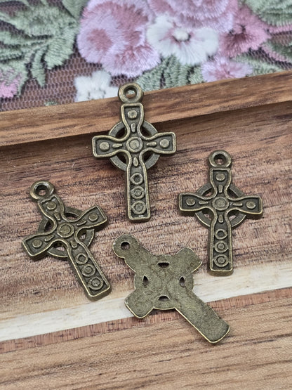 Vier keltische Kreuz-Anhänger in Antikbronze von Vorder- und Rückseite flach liegend auf Holzgrund.