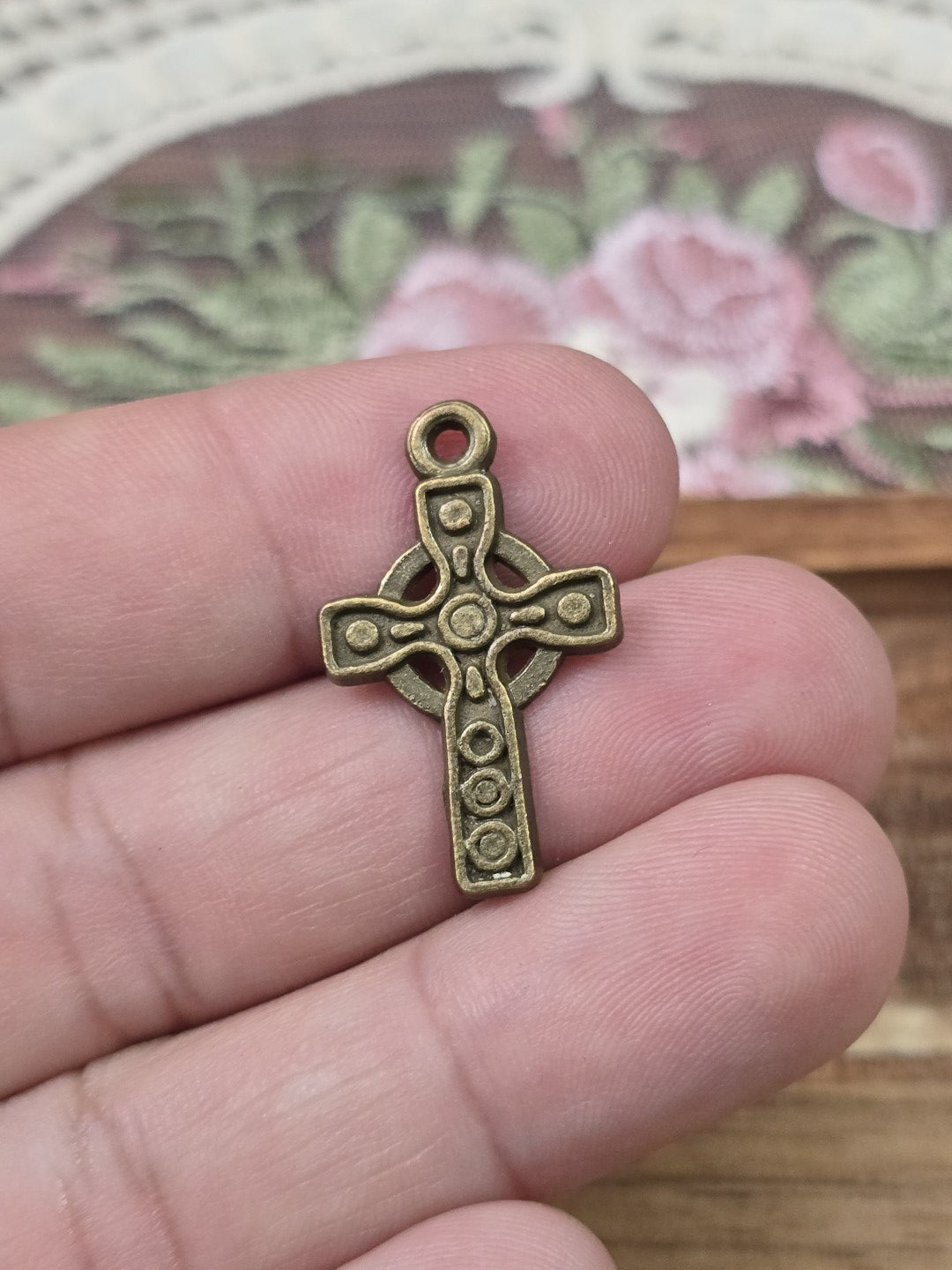 Keltisches Kreuz 26x16mm in Bronze-Optik quer auf Fingern gehalten als Größenvergleich.