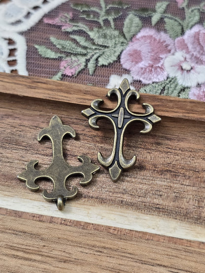 Verzierte Vorderseite und glatte Rückseite der bronze-farbenen Kreuz-Anhänger mit Öse auf Holz.