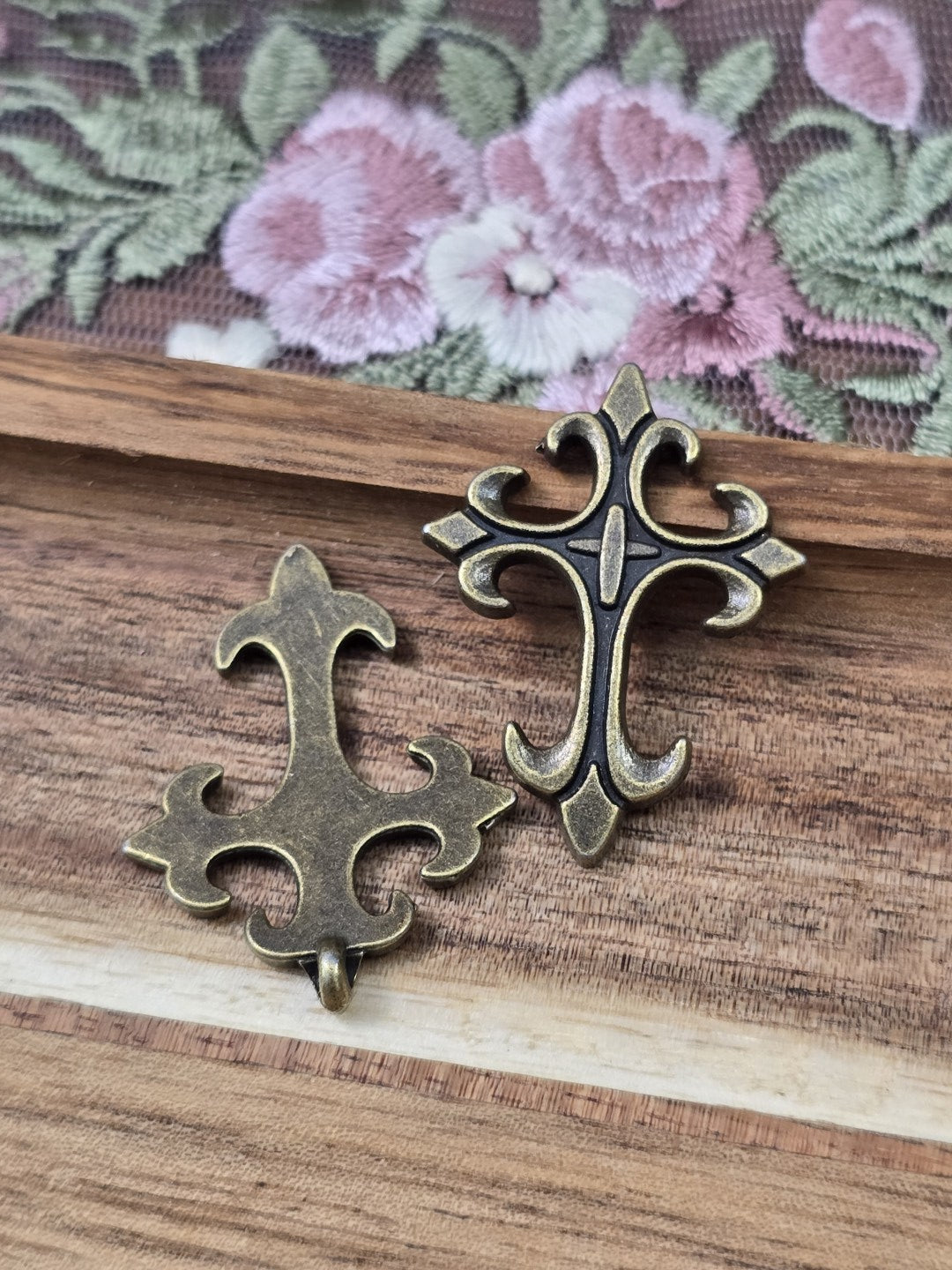 Zwei barocke Kreuz-Schmuckanhänger in Bronze-Optik von beiden Seiten gezeigt.