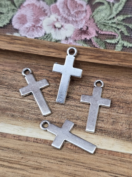 Vier schlichte Kreuz-Anhänger in Antiksilber flach liegend auf Holzgrund.