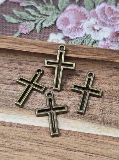 Vier kleine Kreuz-Anhänger mit Rahmendesign in Antikbronze flach liegend auf Holzgrund.