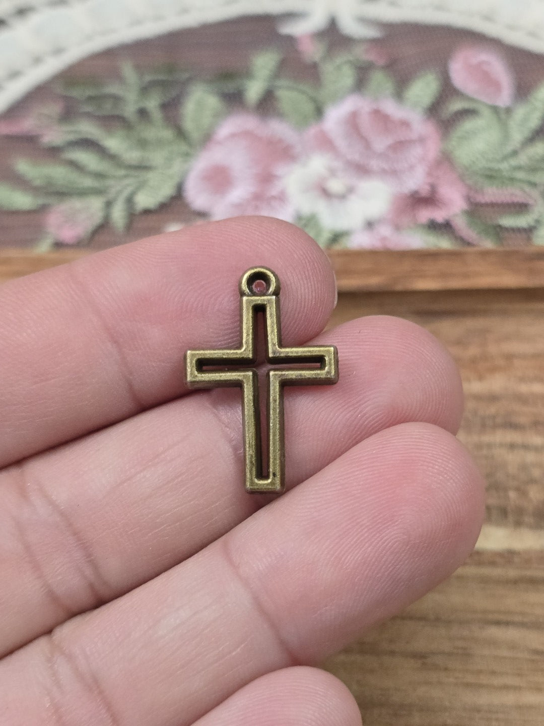 Kleine Kreuz-Charms 17x10mm in Bronze-Optik auf einer Hand gehalten als Größenvergleich.
