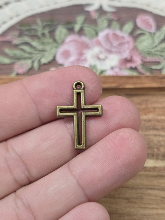 Kleine Kreuz-Charms 17x10mm in Bronze-Optik auf einer Hand gehalten als Größenvergleich.