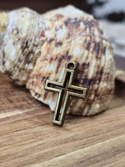 Kreuz-Charm in Antikbronze mit Vertiefung angelehnt an eine Muschel auf Holz für Schmuckdesign.