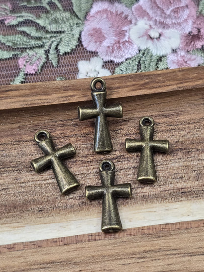 Vier schlichte Kreuz-Anhänger in Antikbronze mit Öse flach liegend auf Holzgrund.