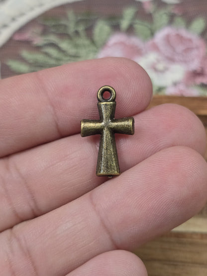 Kleine Kreuz-Perle 20x12mm in Bronze-Optik auf zwei Fingern gehalten als Größenvergleich.