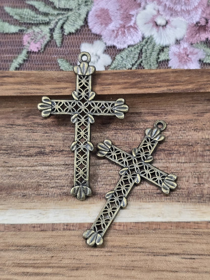 Zwei filigrane Kreuz-Anhänger in Antikbronze mit Lochmuster flach liegend auf Holzgrund.