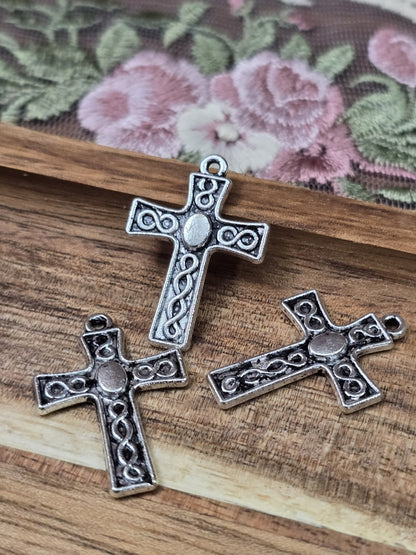 Drei kleine Kreuz-Anhänger in Antiksilber mit keltischem Flechtmuster und Öse flach liegend auf Holzgrund.