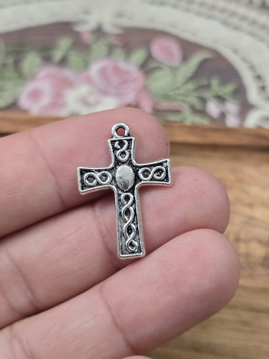 Keltischer Kreuz-Charm 25x18mm in Silber-Optik auf einer Hand gehalten als Größenvergleich.