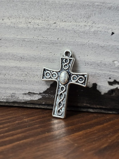 Kreuz-Anhänger in Antiksilber mit Flechtmuster aufrecht stehend vor rustikalem Holz-Hintergrund.