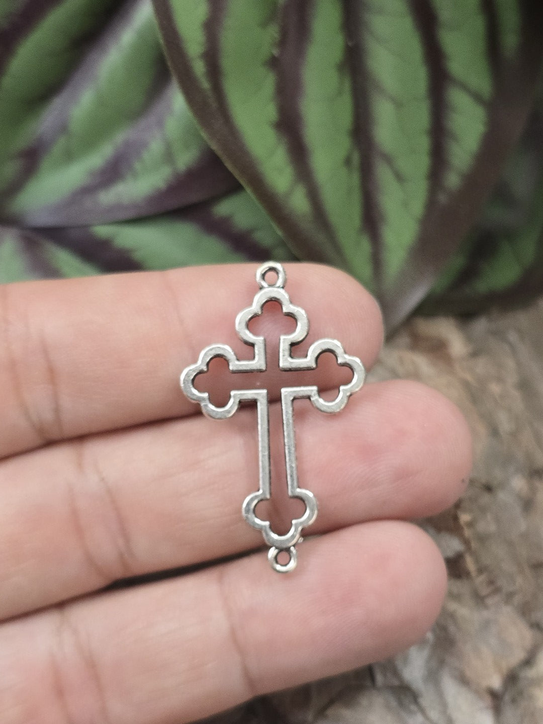 Ein filigranes Gothik-Kreuz als Schmuck-Verbinder in Antik-Silber auf einer Fingerkuppe präsentiert als Größenvergleich.