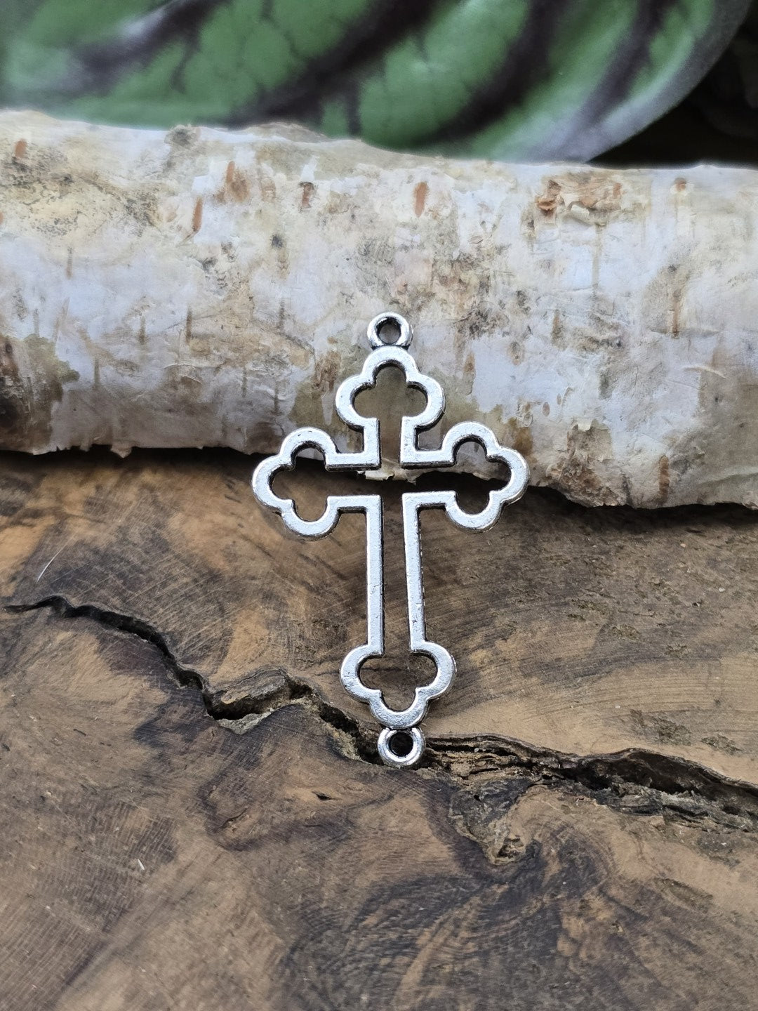 Detailansicht eines einzelnen Kreuz-Verbinders (35 mm) mit zwei Ösen hochkant vor Birkenrinde auf Holzgrund.