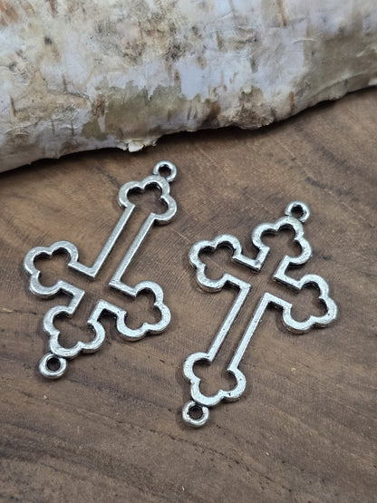 Zwei filigrane Kleeblatt-Kreuz-Verbinder (35 mm) in Antik-Silber flach nebeneinander liegend auf einer Holzplatte.