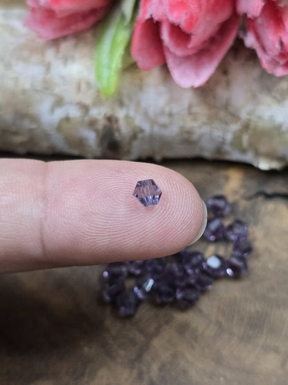 Eine kleine amethystfarbene 4 mm Kristallglas-Bicone-Perle auf einer Fingerkuppe als Größenvergleich.