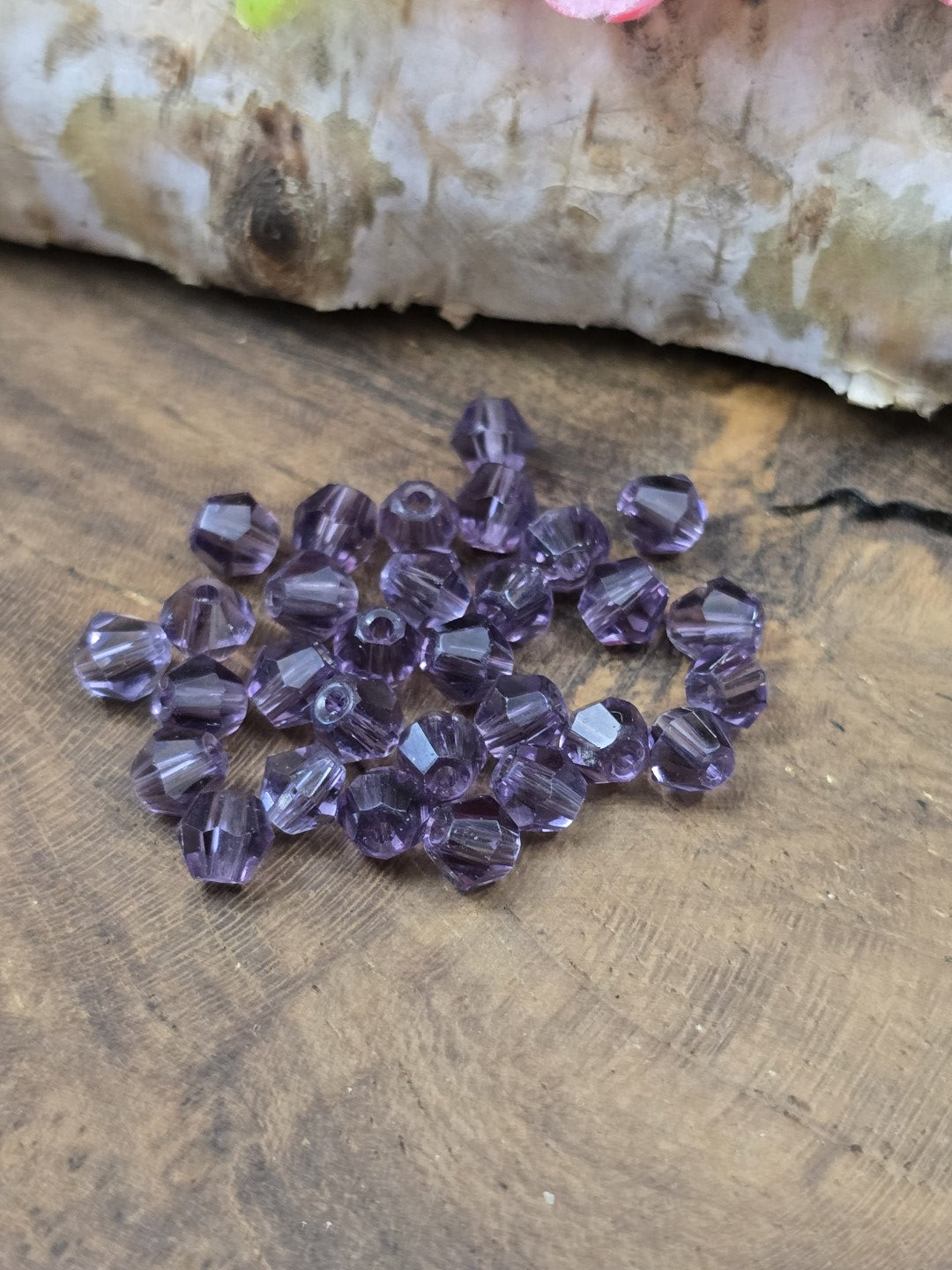 Draufsicht auf geschliffene lilafarbene Kristallglasperlen (4 mm Bicones) mit funkelnden Facetten vor Birkenholz.