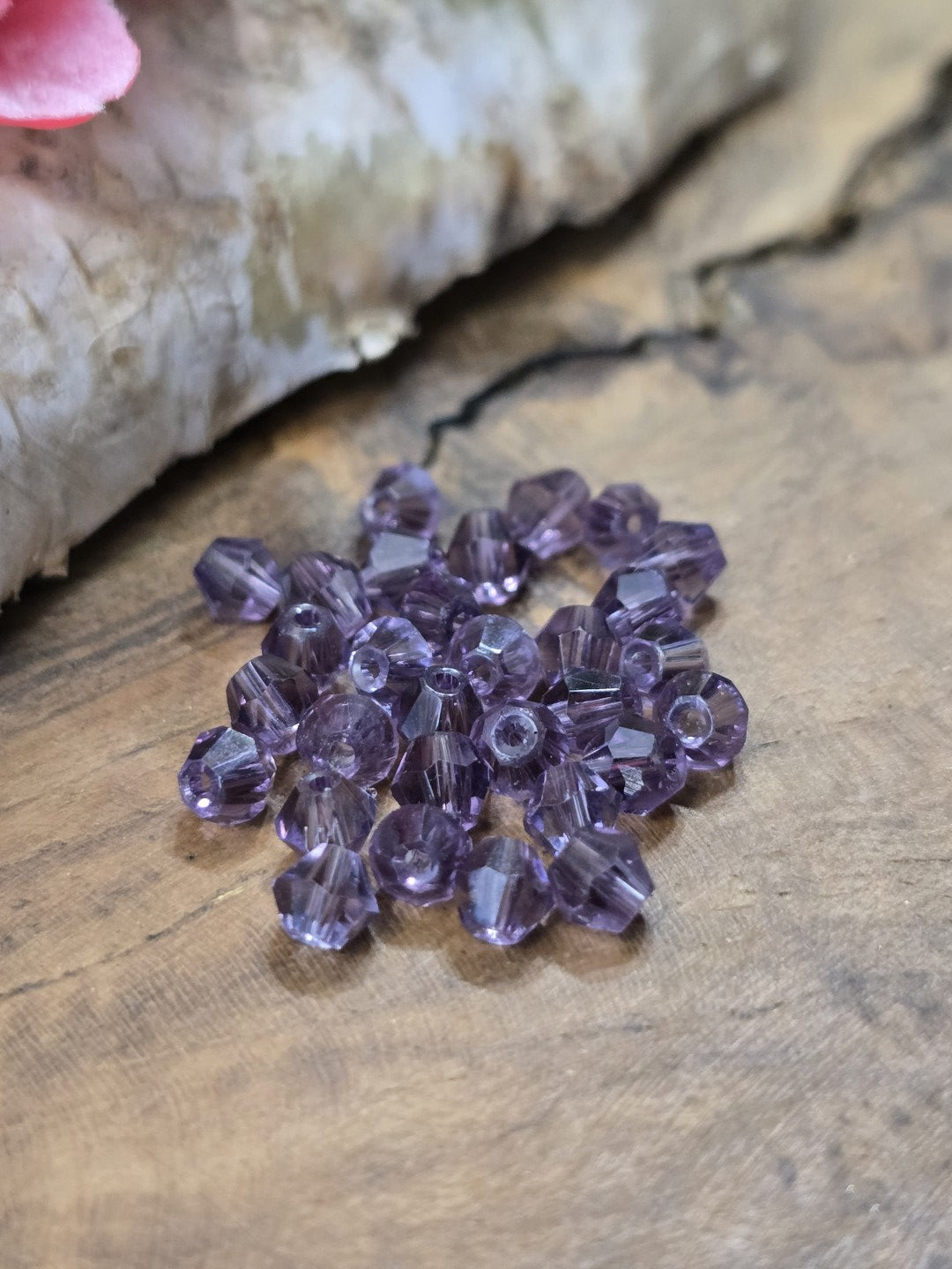 Fokussierte Nahaufnahme von transparenten Amethyst-Kristallglasperlen in Doppelkegelform (4 mm).