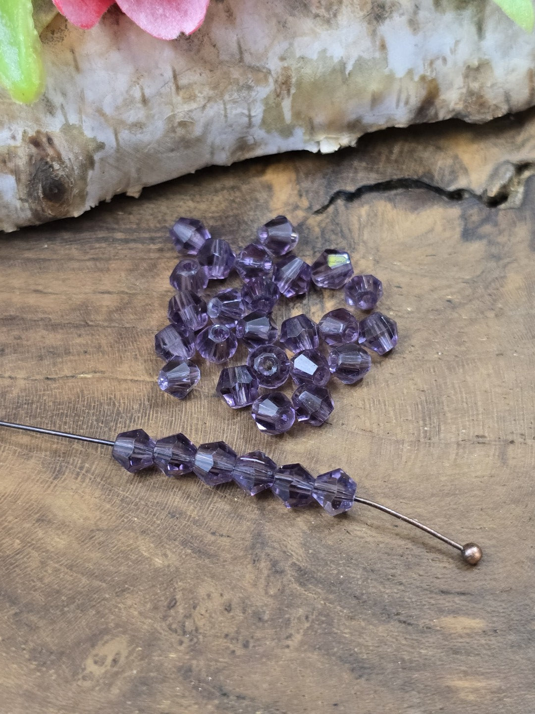 Aufgereihte amethyst-violette 4 mm Kristallglasperlen auf Schmuckdraht zur Demonstration der Fädelbohrung.