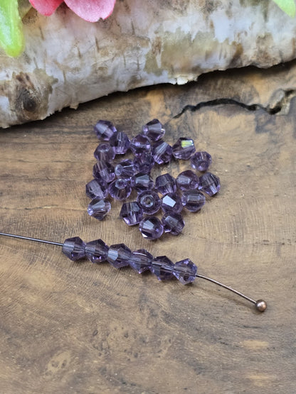 Aufgereihte amethyst-violette 4 mm Kristallglasperlen auf Schmuckdraht zur Demonstration der Fädelbohrung.