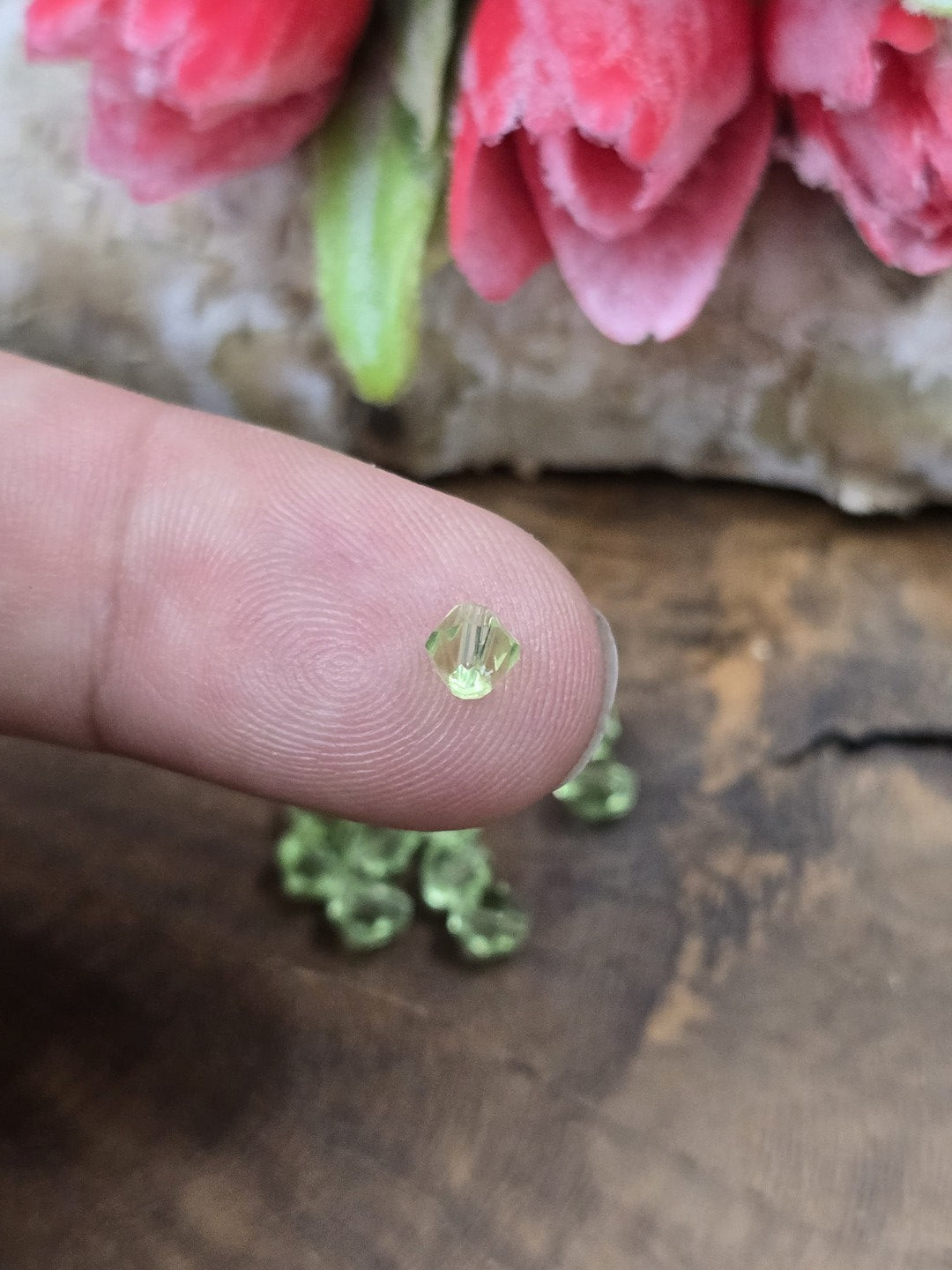 Eine kleine hellgrüne 4 mm Kristallglas-Bicone-Perle auf einer Fingerkuppe als Größenvergleich.