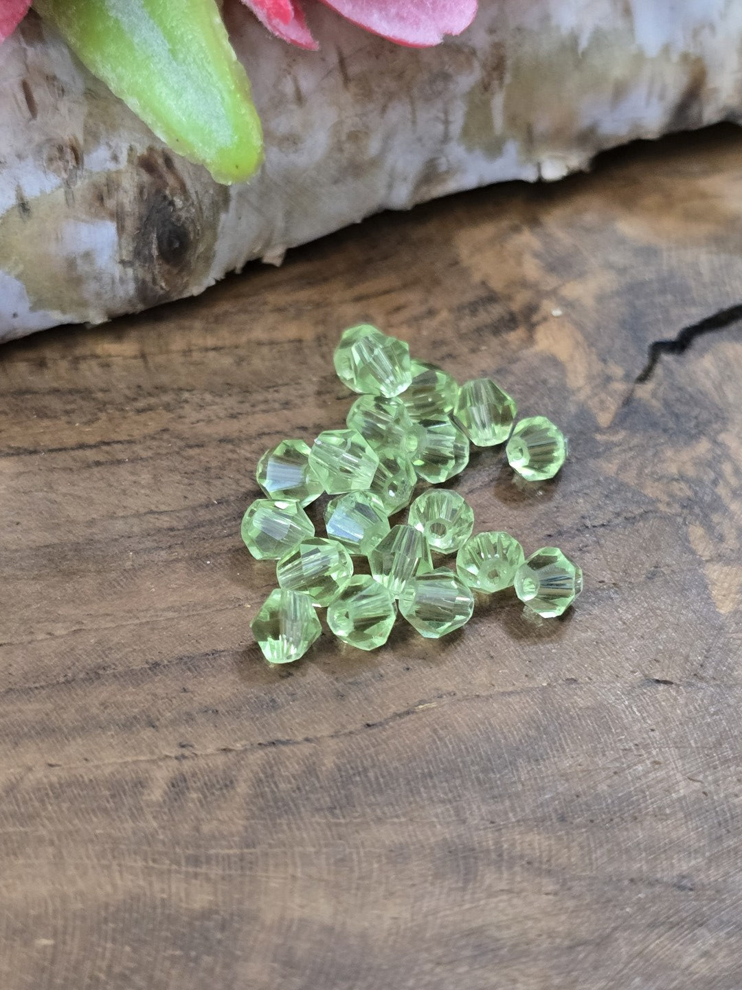 Draufsicht auf transparente hellgrüne Kristallglasperlen (4 mm Bicones) mit funkelnden Facetten vor Birkenholz.