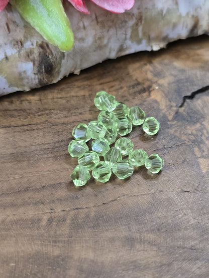 Draufsicht auf transparente hellgrüne Kristallglasperlen (4 mm Bicones) mit funkelnden Facetten vor Birkenholz.