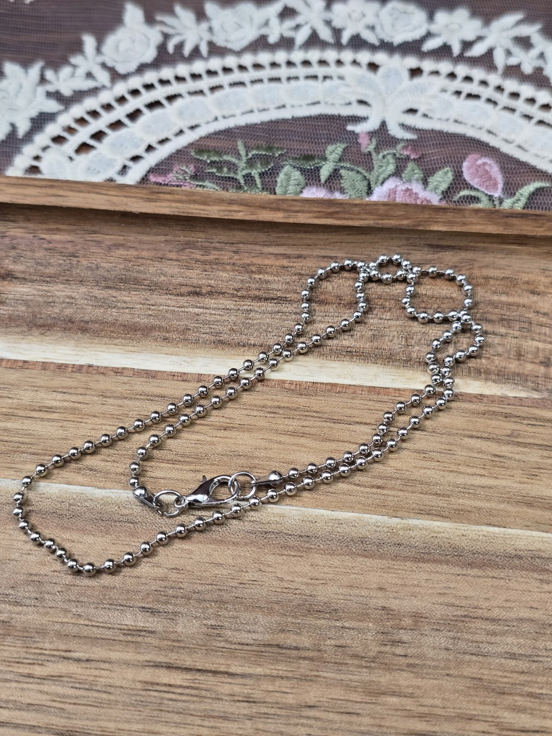 52cm Kugelkette in Dunkelsilber mit Metall-Karabiner ausgelegt auf Holzbrett.