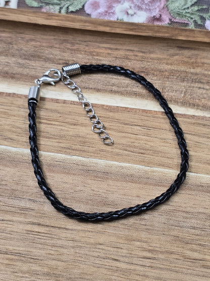 Schwarzes Kunstlederarmband mit Silber-Karabinerverschluss und Verlängerungskette auf Holzgrund.