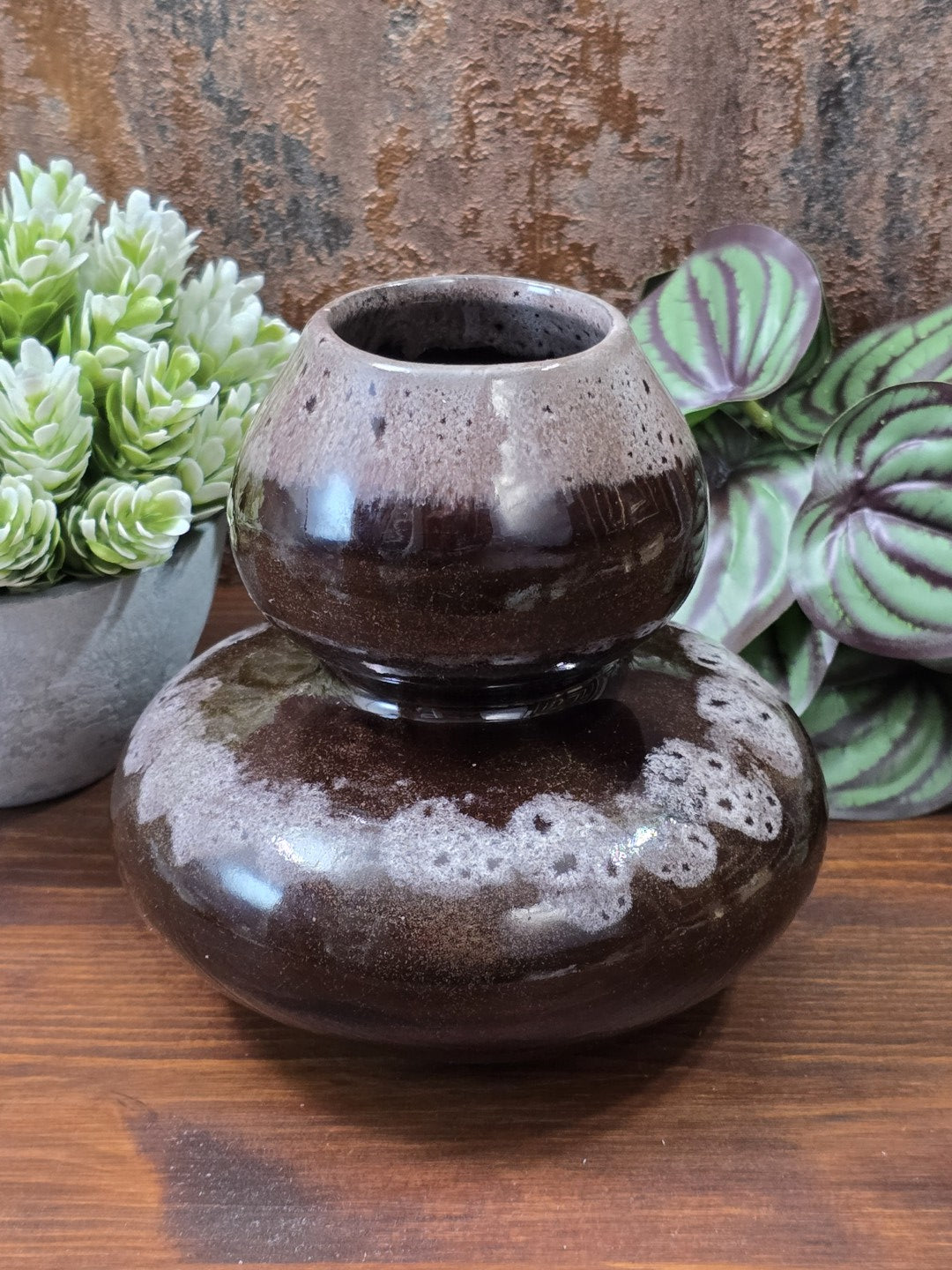 Vintage Keramikvase mit zweigeteilter Kugelform, dunkelbrauner Glasur und hellem Sprenkeldekor vor grünen Pflanzen.
