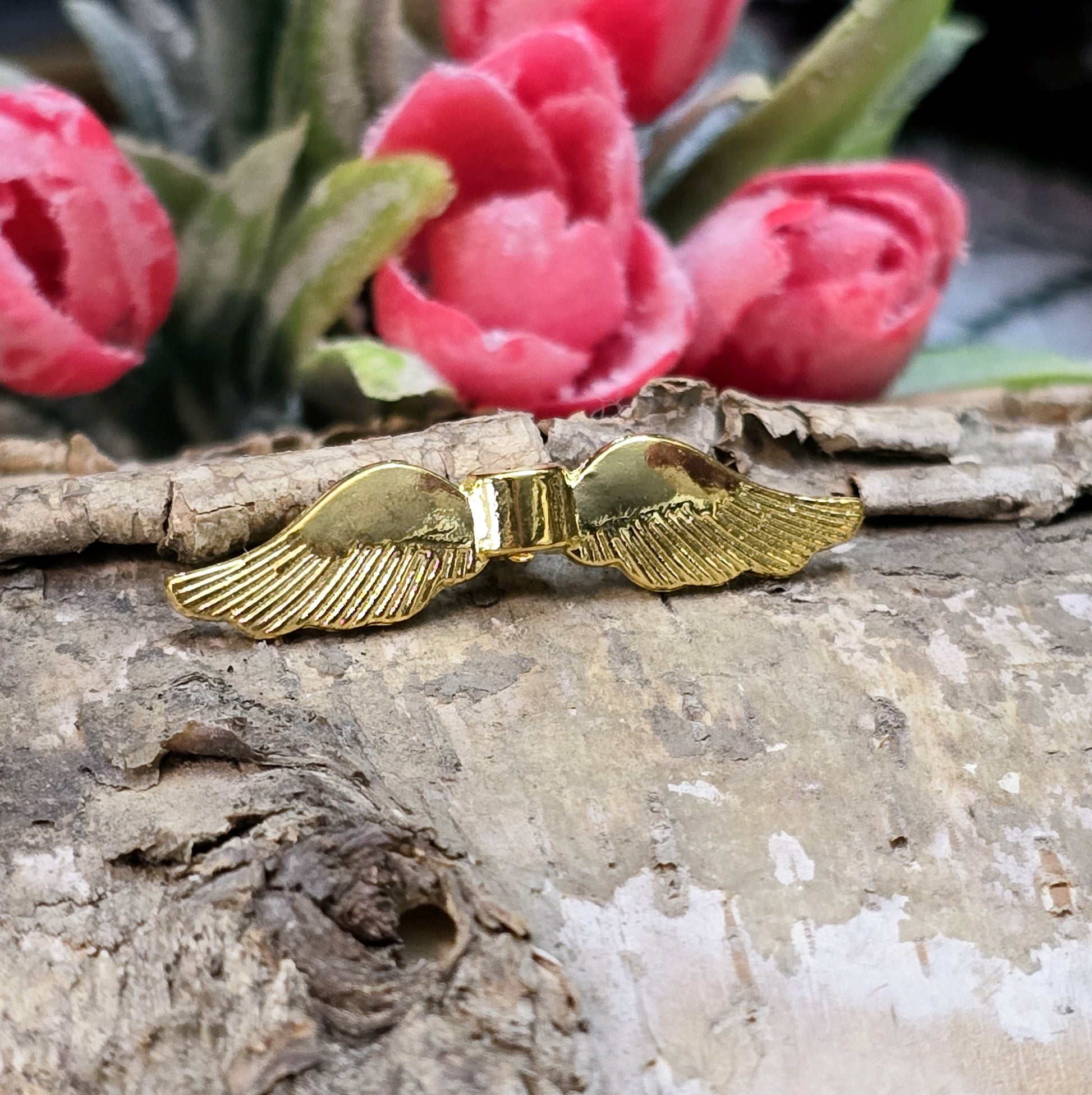 Auf dem Bild ist eine vergoldete Metallperle in Form von Engelsflügeln zu sehen. Mit einer Größe von 35 mm eignet sich diese Perle perfekt für die Gestaltung von Schutzengeln. Die Flügel sind kunstvoll verziert und glänzen in edlem Gold.