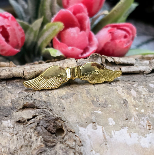 Auf dem Bild ist eine vergoldete Metallperle in Form von Engelsflügeln zu sehen. Mit einer Größe von 35 mm eignet sich diese Perle perfekt für die Gestaltung von Schutzengeln. Die Flügel sind kunstvoll verziert und glänzen in edlem Gold.