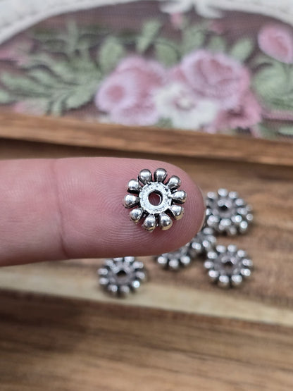 Silberfarbene Zwischenperle in Zahnrad-Optik 10mm auf einer Fingerkuppe als Größenvergleich.