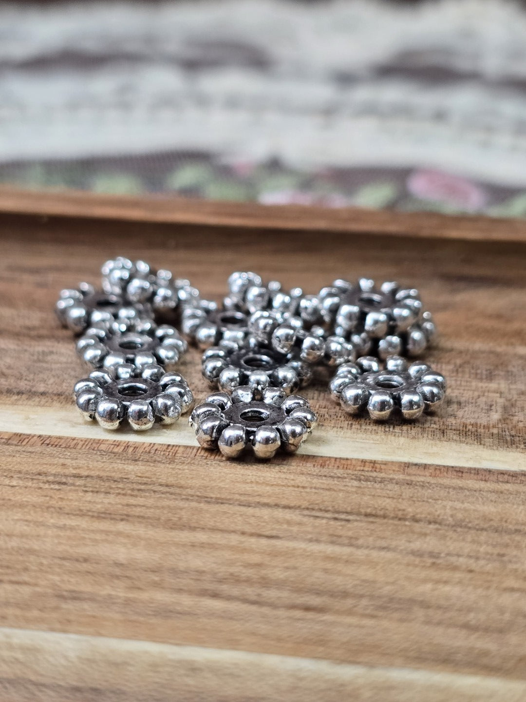 Blütenförmige Metall-Spacer in Silber flach liegend auf Holzgrund für Schmuckherstellung.