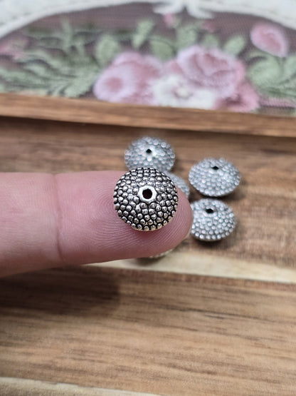 Silberne Ufo-Metallperle 11mm mit strukturierter Oberfläche auf einer Fingerkuppe als Größenvergleich.