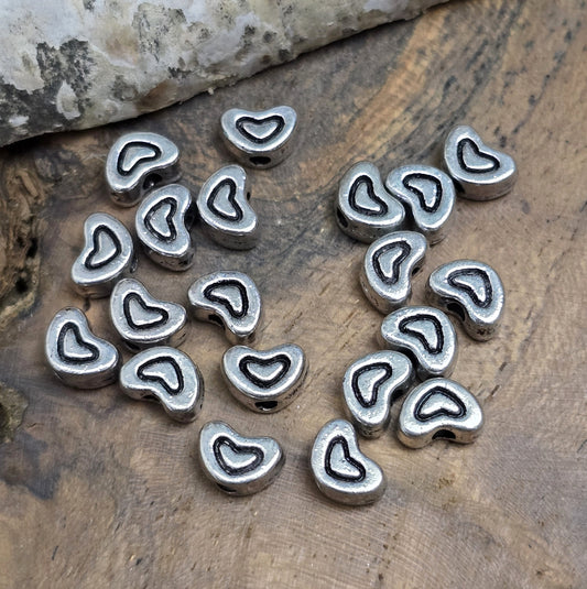 20 kleine Metallperlen in Herzform, antiksilberfarben, mit feinen Intarsien. Größe: 5 x 7 mm. Ideal für Schmuckprojekte wie Armbänder und Ketten. Das Fädelloch verläuft längs und erleichtert das Auffädeln auf verschiedene Drähte. Menge: 20 Stück.