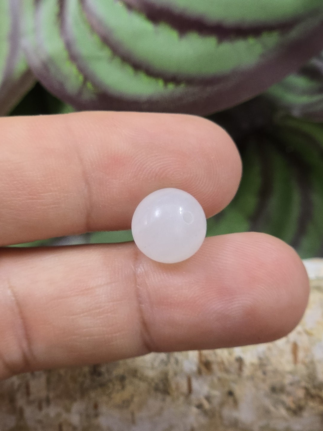 Weiße Milchquarz-Perle mit 10 mm Durchmesser auf den Fingern als Größenvergleich
