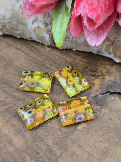 Vier rechteckige gelbe Millefiori-Glasperlen (14x10 mm) mit buntem Blumenmuster flach auf Holzgrund platziert.