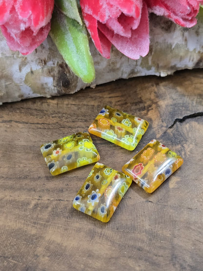 Nahaufnahme von vier flachen Millefiori-Glasperlen in Gelb mit bunten Blumenmotiven für DIY-Schmuck.