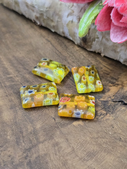 Draufsicht auf vier gelbe rechteckige Motivperlen (14x10 mm) aus Glas vor Birkenholz-Hintergrund.