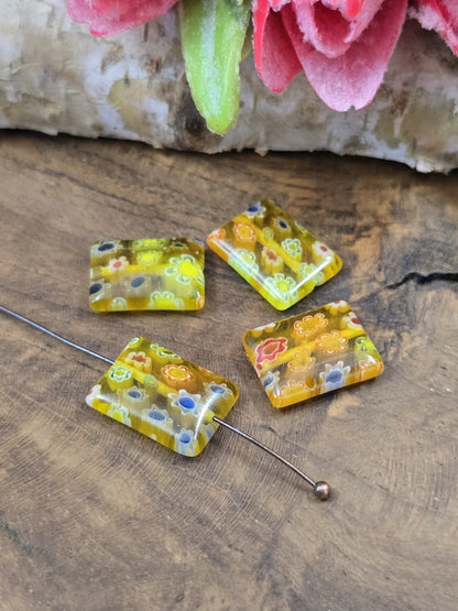 Gelbe Millefiori-Glasperle auf einen Nietstift aufgereiht neben drei weiteren Perlen zur Veranschaulichung der Bohrung.