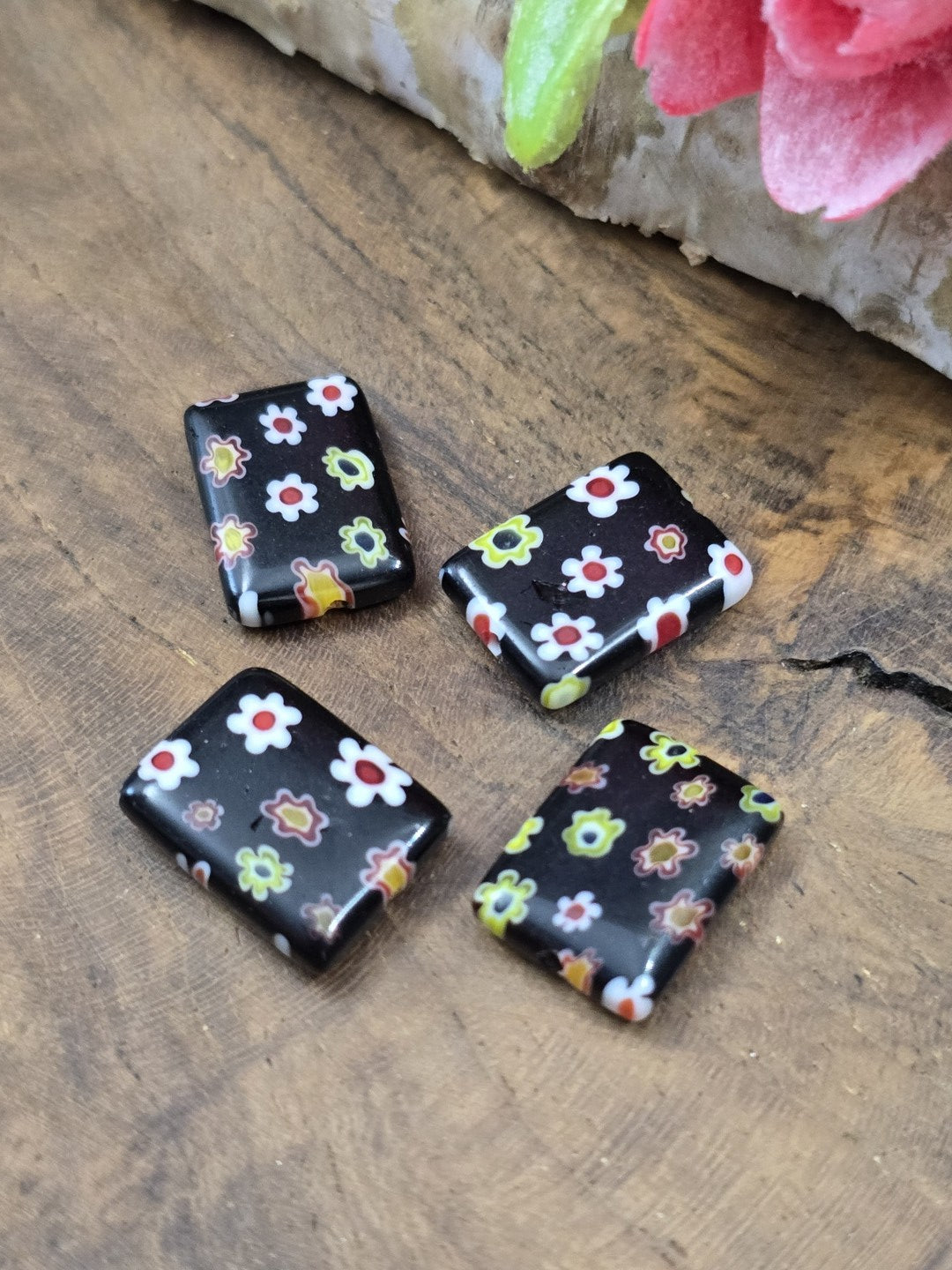 Nahaufnahme von vier flachen Millefiori-Glasperlen in Schwarz mit bunten Blumenmotiven für DIY-Schmuck.