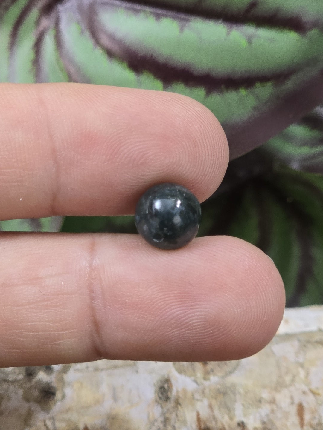 Dunkelgrüne Moosachat-Perle mit 8 mm Durchmesser auf den Fingern als Größenvergleich