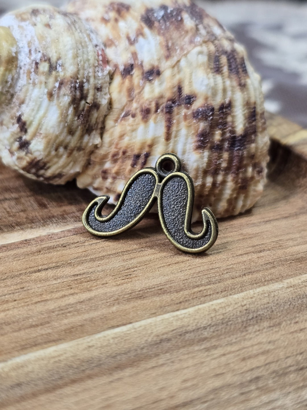 Schnurrbart-Charm in Antikbronze angelehnt an eine Muschel auf Holz für Schmuckdesign.