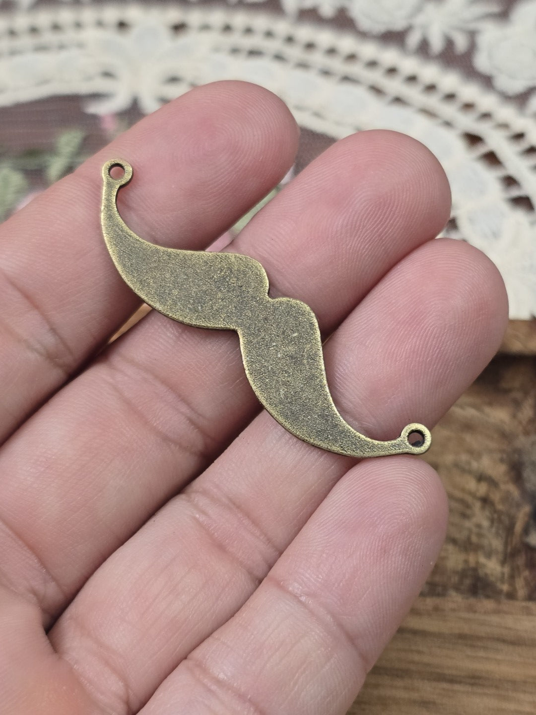 Oberlippenbart-Zwischenstück 49mm in Bronze-Optik auf einer Hand gehalten als Größenvergleich.
