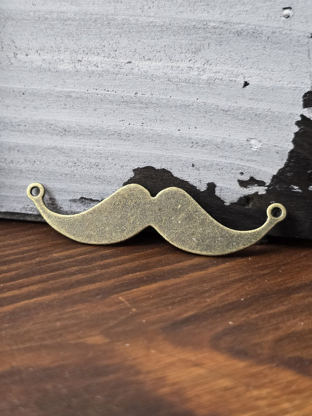 Schnurrbart-Zwischenelement in Vintage-Bronze stehend vor rustikalem Holz-Hintergrund für Schmuckherstellung.