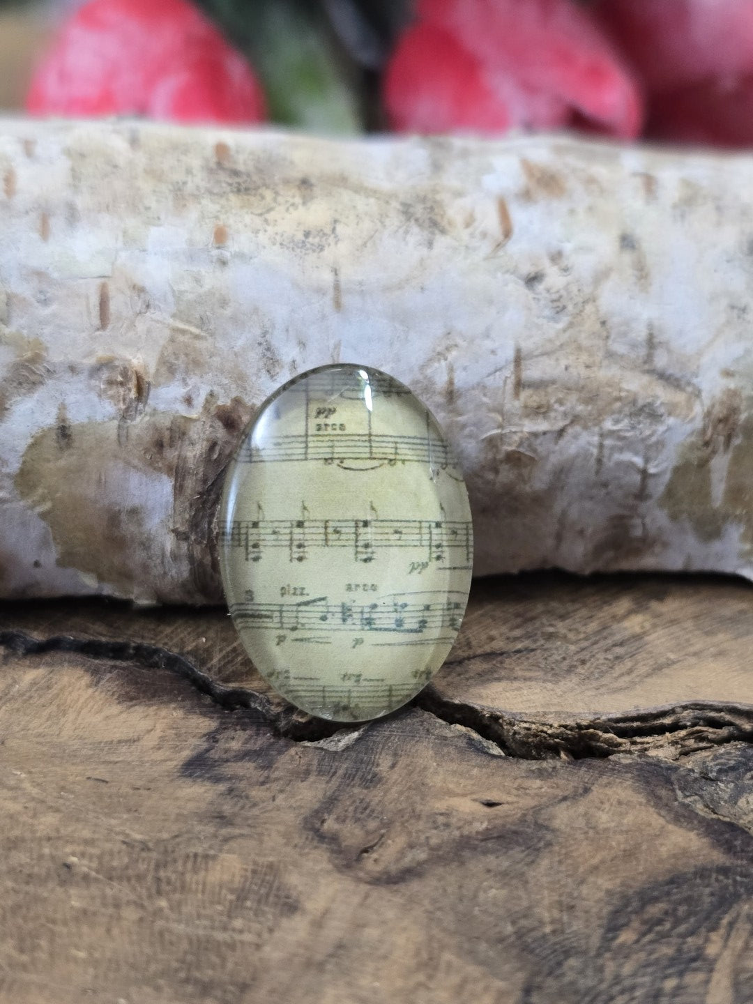 Nahaufnahme eines einzelnen 18x13 mm großen ovalen Glascabochons mit filigranem Noten-Motiv als Schmuckzubehör zum Basteln von Medaillons, Ringen oder Ketten.