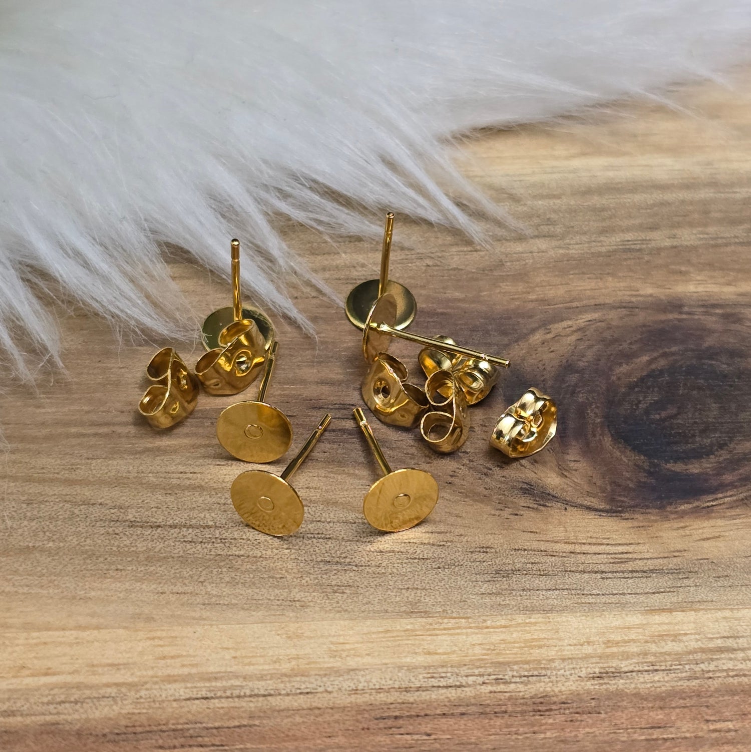 Das Bild zeigt Ohrstecker mit runder Klebeplatte aus Edelstahl in gold mit Flügelmuttern.